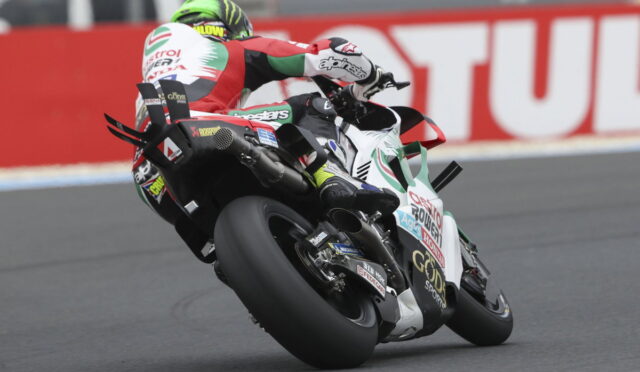Motorcycle racer wearing red, white, and green leans into a turn on a sportbike during a race.