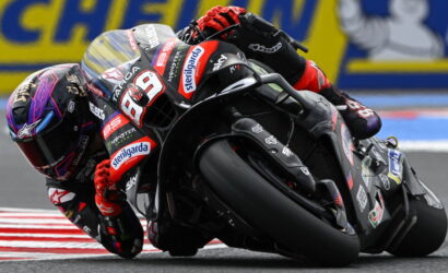 MotoGP rider in red-and-black leathers leaning into a turn on a race track, bike number 93 with sponsor logos.