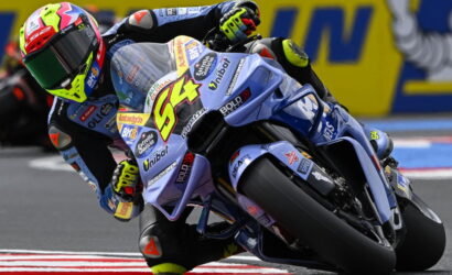 Motorcycle racer in a bright helmet leaning into a turn on a blue racing bike during a race (number 84).