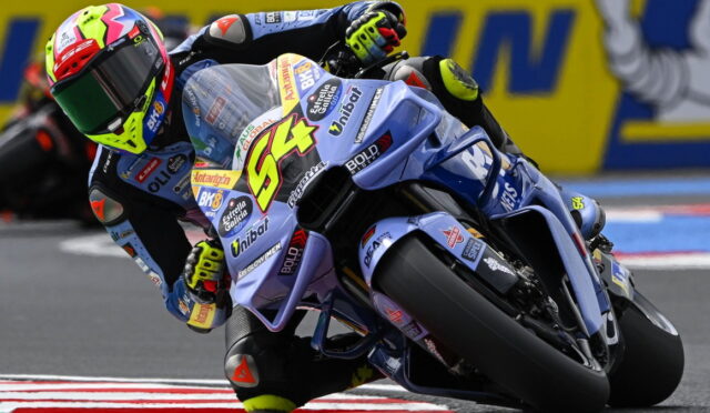 Motorcycle racer in a bright helmet leaning into a turn on a blue racing bike during a race (number 84).