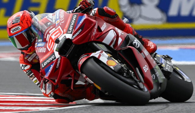 MotoGP rider in red suit and helmet leaning into a sharp corner on a red Ducati bike with sponsor decals (Lenovo, Shell) in a race track setting