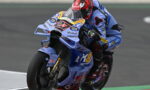 Rider in blue racing suit on a blue sport bike leaning into a turn during a race, number 48 on the bike plate.