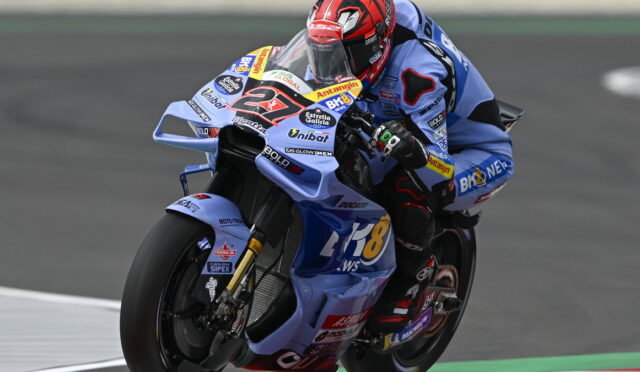 Rider in blue racing suit on a blue sport bike leaning into a turn during a race, number 48 on the bike plate.