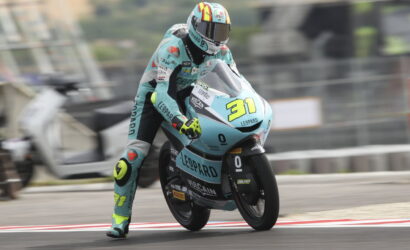 Motorcycle racer in teal livery leans into a track turn on a racing bike number 31 with Leopard branding.