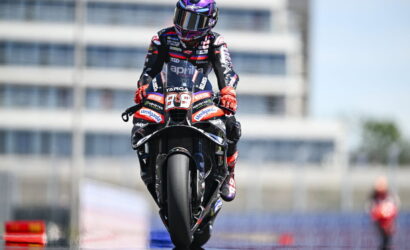 Rider in full racing gear on a sport motorcycle with the number 89, speeding on a track under a clear sky.