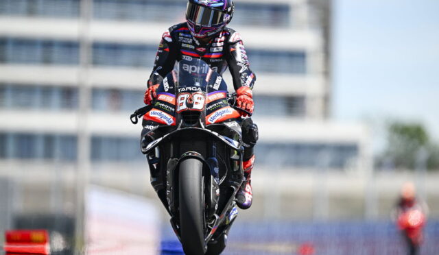 Rider in full racing gear on a sport motorcycle with the number 89, speeding on a track under a clear sky.