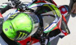 Motorsport rider holding a bright green helmet while seated on a racing motorcycle with Castrol branding and red bodywork