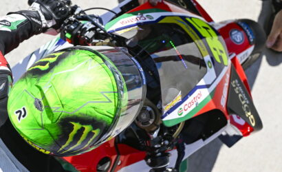 Motorsport rider holding a bright green helmet while seated on a racing motorcycle with Castrol branding and red bodywork