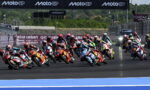 Group of colorful MotoGP riders lean into a sharp turn on a racetrack, banners reading MotoGP and Qatar Airways in the background.