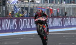 Motorcycle racer lifts front wheel on a race track, performing a wheelie with a sponsor-laden bike and Qatar Airways banners in the background.
