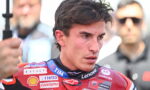 Close-up of a male motorcycle racer in a red sponsor-labeled racing suit with a focused expression.