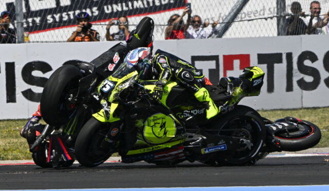 Motorcycle race crash: rider in neon yellow gear slides along the track beside another bike as spectators watch from behind barriers.