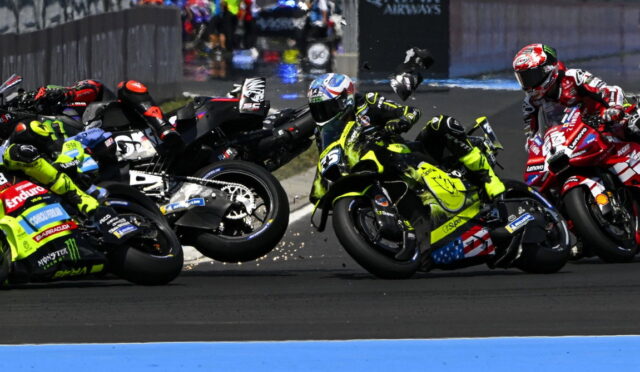 Motorcycle racers lean into a sharp corner in a crowded race, sparks flying as bikes slide wheels side-by-side across the track.