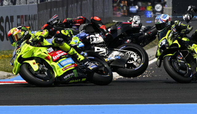 Group of motorcycle racers lean into a sharp turn on a racetrack, wearing bright yellow-green suits and helmets; sparks fly from the tires.