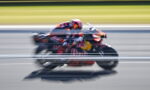 Racing motorcycle with red livery speeding on a track, motion blur suggesting high speed.