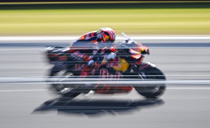 Racing motorcycle with red livery speeding on a track, motion blur suggesting high speed.