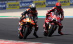 Two motorcycle racers lean into a left-hand curve on a race track, bike numbers 37 and 99 leading the pack.
