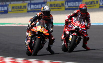 Two motorcycle racers lean into a left-hand curve on a race track, bike numbers 37 and 99 leading the pack.