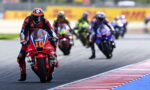 Motorcycle racer number 10 leads a pack on a race track with riders blurred in the background on a curve.