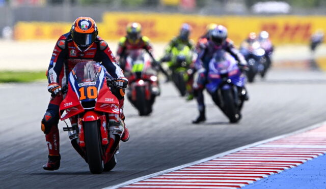 Motorcycle racer number 10 leads a pack on a race track with riders blurred in the background on a curve.