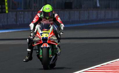 Motorcycle racer in red, white, and green gear riding on a racetrack toward the camera, neon green helmet with number 35 on the bike's front fairing.