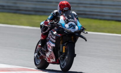 Racer in a red helmet leaning into a turn on a blue-and-white race bike number 95, with sponsor decals on a racetrack surface.