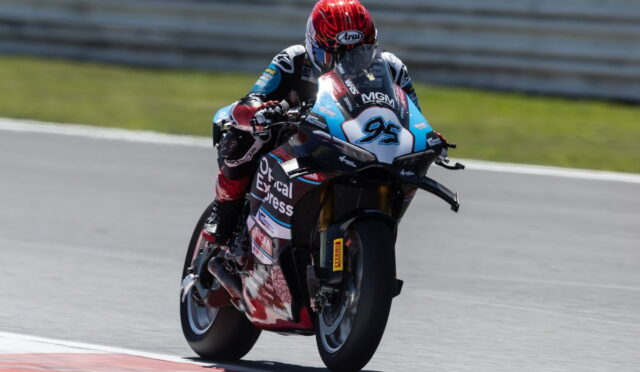 Racer in a red helmet leaning into a turn on a blue-and-white race bike number 95, with sponsor decals on a racetrack surface.