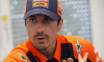 Close-up of a man in an orange KTM/Red Bull racing cap and matching racing jersey, looking to the side as if talking or listening.