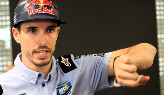 Portrait of a man wearing a Red Bull cap and light blue racing shirt, extending his fist toward the camera.