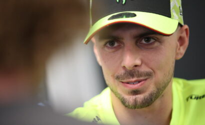 Close-up of a man wearing a neon yellow cap and shirt, looking at someone off-camera while speaking.