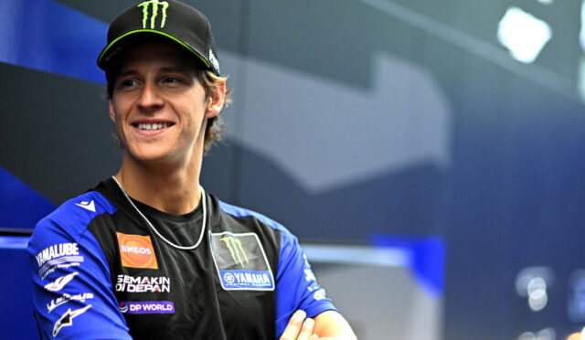 Smiling male motorcycle racer in a blue Yamaha team jersey and black Monster Energy cap.
