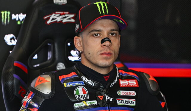 Motorcycle racer in a sponsor-loaded racing suit sitting in a high-backed cockpit seat, wearing a Monster cap.