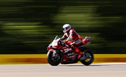 Rider in red racing suit on a red Ducati sport motorcycle speeding along a track with a motion-blurred background, helmeted rider leaned forward.