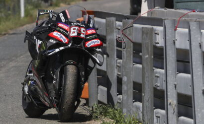 Racing motorcycle leaning into a metal barrier on a track, front tire dusty from the road surface.