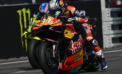 Motorcycle racer leaning into a turn on a KTM race bike with Red Bull livery, Monster energy backdrop in the background.