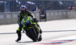 Motorcycle racer in a neon yellow-green suit leaning into a turn on a race track with a blue-red helmet.
