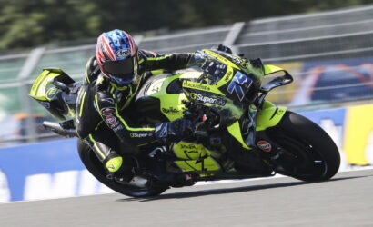 Two motorcycle racers lean deeply into a turn on a racetrack, neon-yellow bikes and matching gear dominating the scene.
