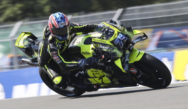 Two motorcycle racers lean deeply into a turn on a racetrack, neon-yellow bikes and matching gear dominating the scene.