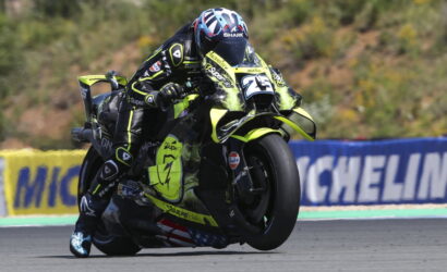 Motorcycle racer in neon yellow suit leaned into a turn on a race track, number 25, helmeted and riding a matching neon bike.
