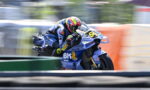 Motorcycle racer leaning into a curve on a blue Ducati bike, neon yellow helmet, speed-blurred background.
