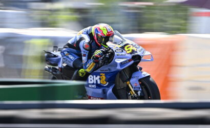 Motorcycle racer leaning into a curve on a blue Ducati bike, neon yellow helmet, speed-blurred background.