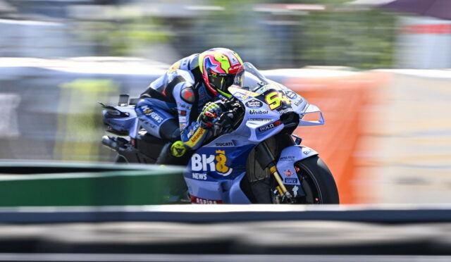 Motorcycle racer leaning into a curve on a blue Ducati bike, neon yellow helmet, speed-blurred background.
