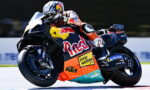 MotoGP rider in orange suit leaning into a turn on a Red Bull KTM race bike with sponsor decals visible (Interwetten, Michelin, Motorex).
