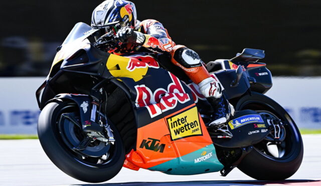 MotoGP rider in orange suit leaning into a turn on a Red Bull KTM race bike with sponsor decals visible (Interwetten, Michelin, Motorex).