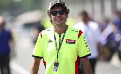 Man wearing a neon yellow Enduro team shirt, black sunglasses, and a cap with Monster logo at an outdoor event; lanyard with badge hanging from neck.