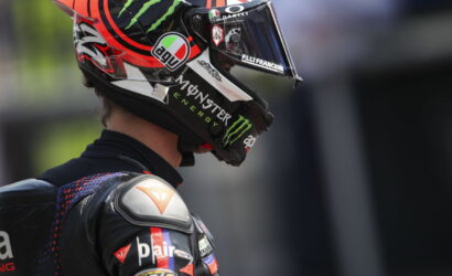 Side profile of a motorcycle racer wearing a black and red helmet with Monster Energy and sponsor logos.