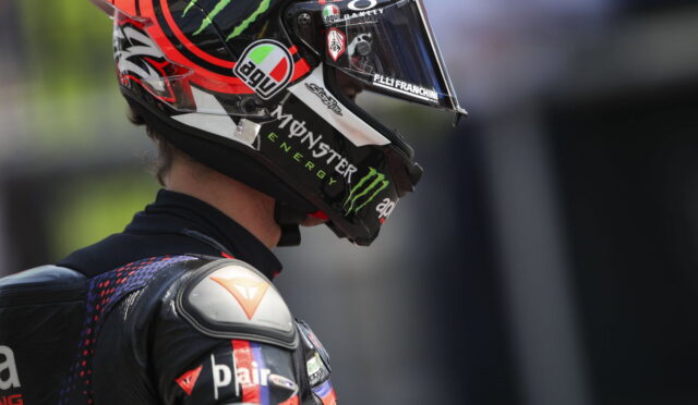Side profile of a motorcycle racer wearing a black and red helmet with Monster Energy and sponsor logos.