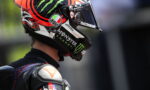 Side profile of a motorcycle racer wearing a helmet with Monster Energy branding and sponsor decals on a black racing suit.