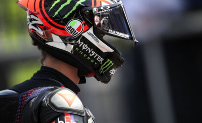 Side profile of a motorcycle racer wearing a helmet with Monster Energy branding and sponsor decals on a black racing suit.