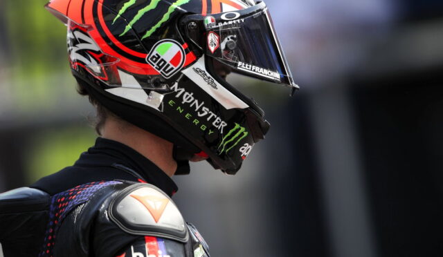 Side profile of a motorcycle racer wearing a helmet with Monster Energy branding and sponsor decals on a black racing suit.